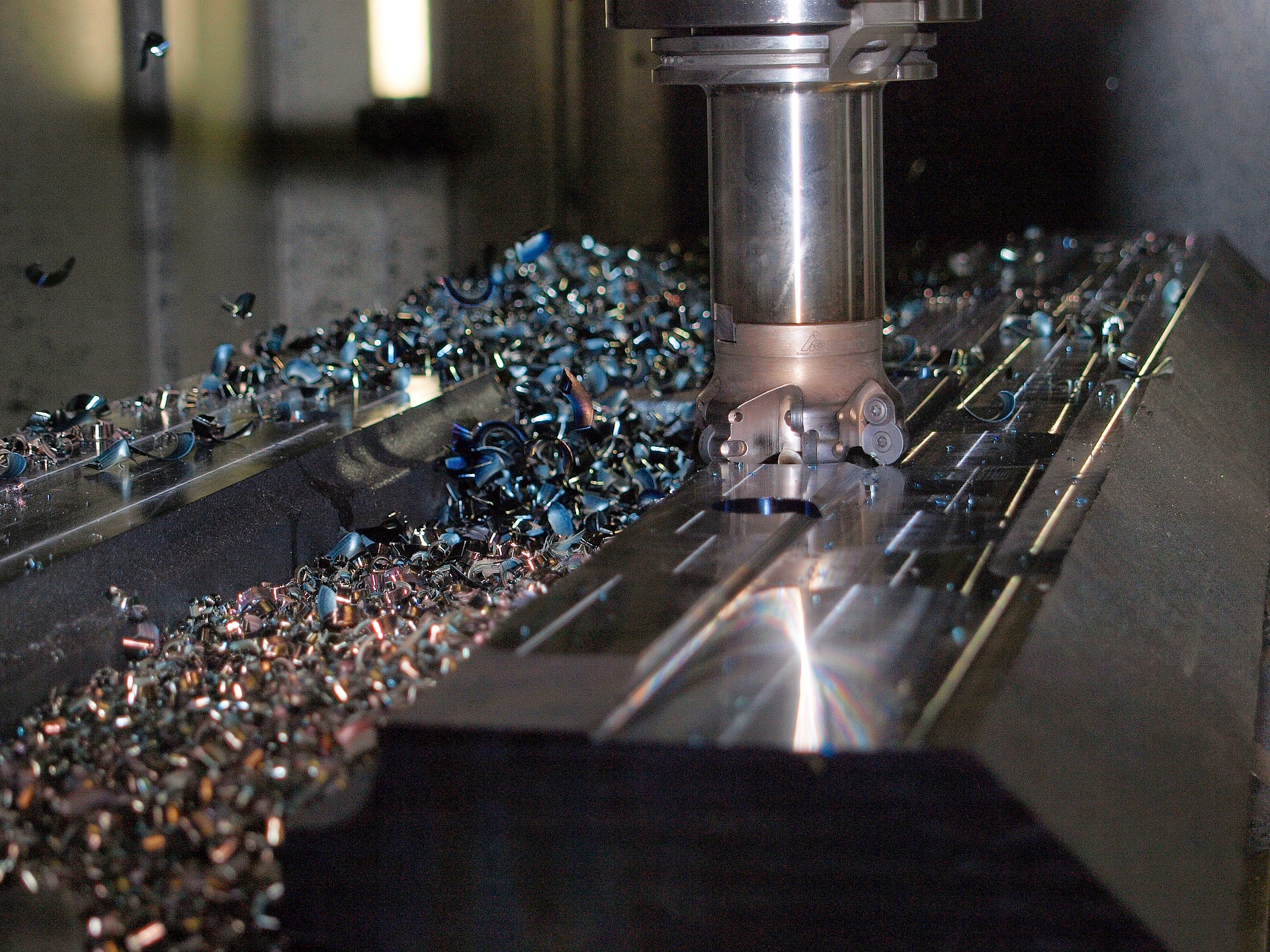 Eine Fräsmaschine bearbeitet ein Metallwerkstück. Metallspäne in verschiedenen Farben und Formen liegen auf und neben dem Werkstück. Die Oberfläche des Metalls glänzt, und die Fräse ist im Arbeitsprozess zu sehen.