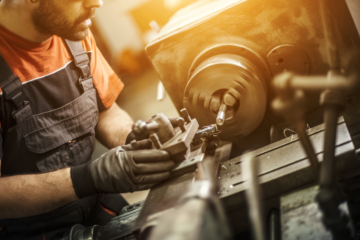 Mann mit Handschuhen bedient eine Drehmaschine in Werkstatt